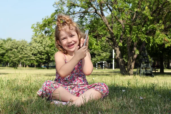 Маленька дівчинка сидить на траві і грає з планшетом — стокове фото