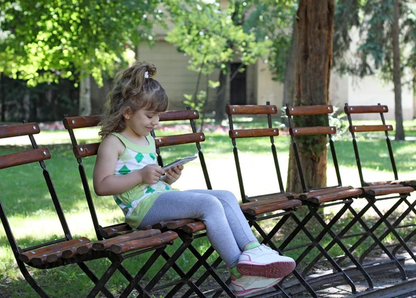 Liten flicka med tablett sitter i parken — Stockfoto
