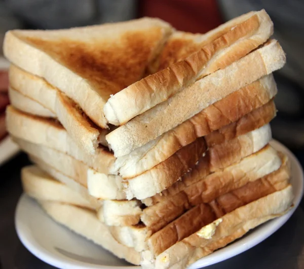 Mucchio di pane tostato imburrato su un piatto bianco — Foto Stock