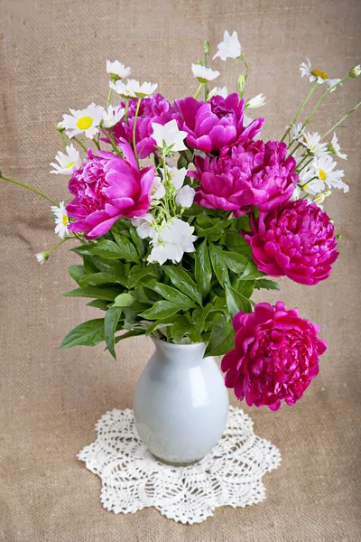 Bouquet of peonies and daisies in a white vase on a lace napkin — Stock Photo, Image