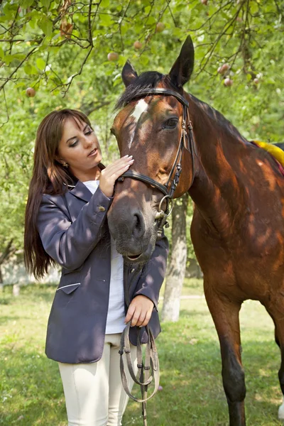 Молодая женщина идет с лошадью в яблоневом саду — стоковое фото