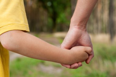 Mother holding a hand of his son outdoors clipart