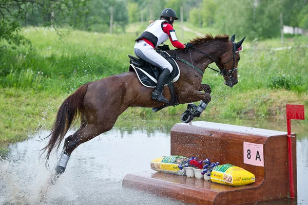 Woman eventer on horse is overcomes the fence in water — Stock Photo, Image