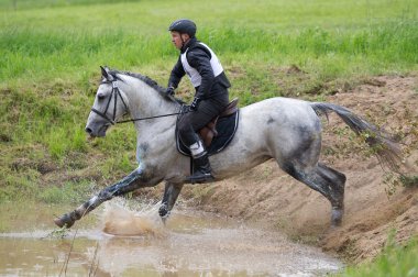 Eventer on horse negotiating Water jump clipart