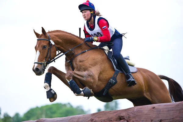 Desporto equestre. Mulher eventer em cavalo negociando cross-country Obstáculo fixo Cerca de registro — Fotografia de Stock