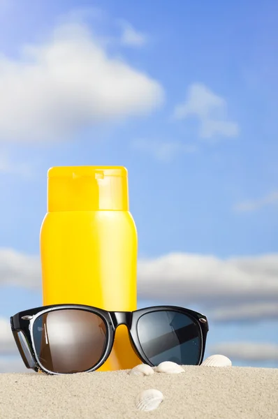 Tube with sun protection and sunglasses on beach — Stock Photo, Image