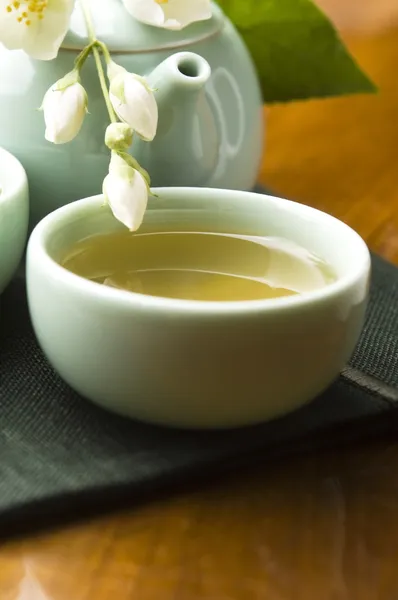 Зеленый чай с жасмином в чашке и чайник на деревянном столе — стоковое фото