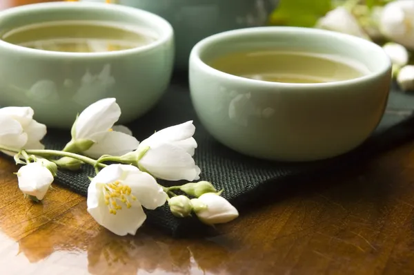 Grönt te med jasmine i kopp och tekanna på träbord — Stockfoto