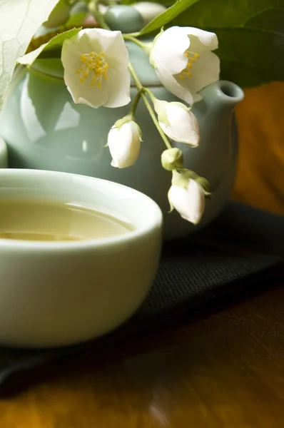 Зеленый чай с жасмином в чашке и чайник на деревянном столе — стоковое фото