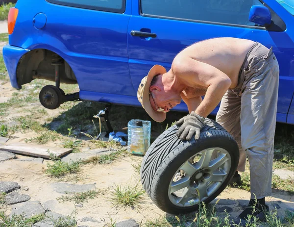 Старший чоловік змінює колесо своєї машини — стокове фото