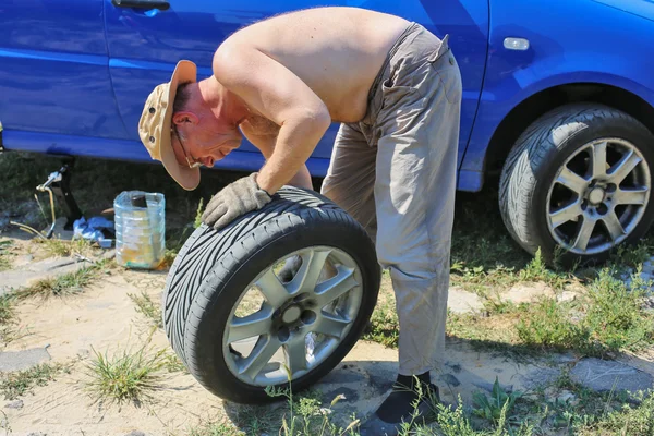 Старший человек меняет колесо своей машины — стоковое фото