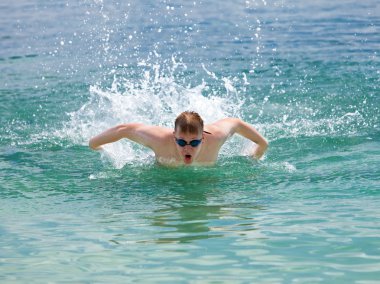 Young sporting man swims in the sea dolphin style. clipart