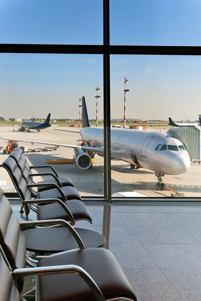 Poltronas vazias na sala de espera do aeroporto e avião atrás da janela — Fotografia de Stock