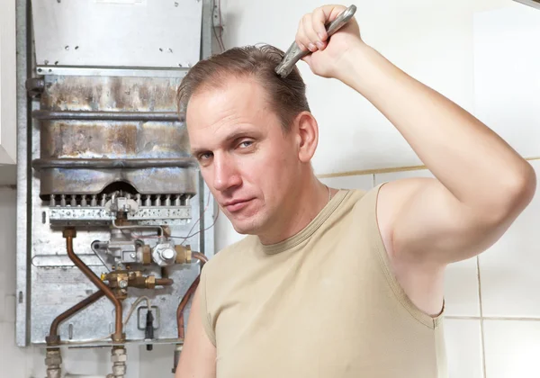 El hombre con una llave inglesa piensa en la reparación de un calentador de agua a gas — Foto de Stock