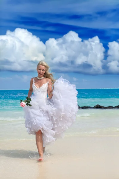 A bela mulher jovem em um vestido da noiva na borda do mar com uma rosa em uma mão — Fotografia de Stock