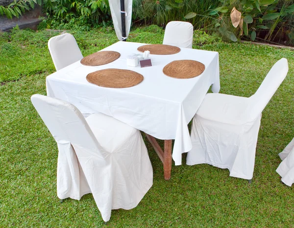 Table with a white cloth and 4 chairs on a green lawn — Stock Photo, Image