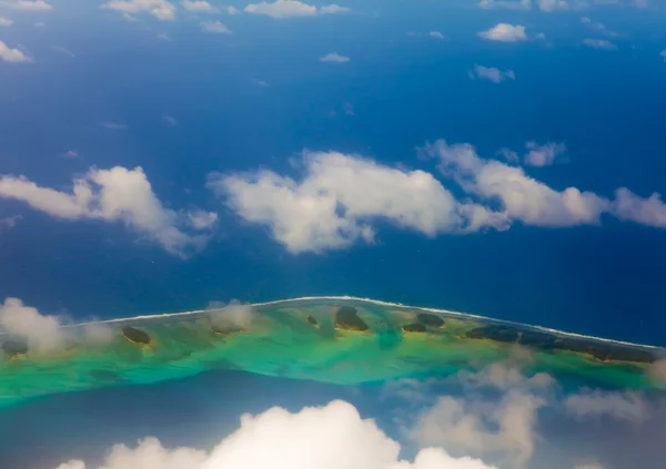 Atol ring v oceánu je viditelný skrz mraky. Letecký pohled. — Stock fotografie