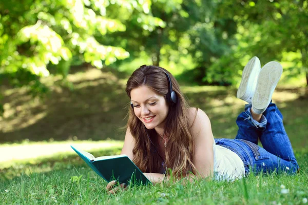 Mladá žena s headsetem čtení knih v parku — Stock fotografie