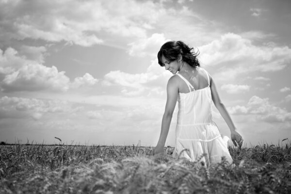 Young woman walking through wheat field touching wheat, black and white