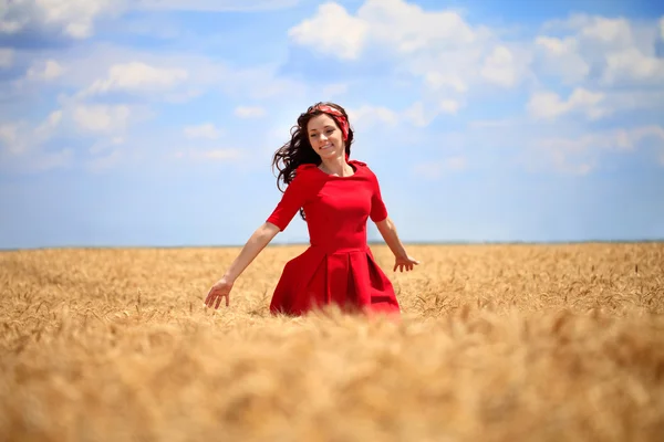 Chica en un vestido rojo caminando por el campo de trigo . —  Fotos de Stock