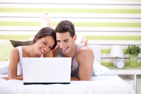 Mladý pár, pomocí přenosného počítače, zatímco ležel na posteli — Stock fotografie