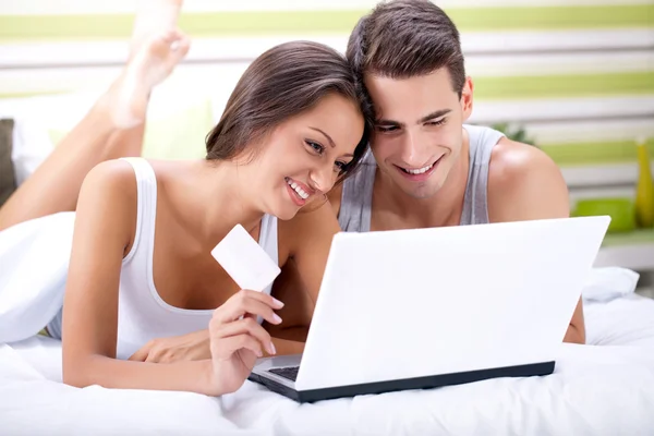 Sorrindo casal compras on-line enquanto deitado em sua cama — Fotografia de Stock