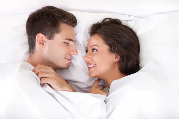 Pár leží v posteli s úsměvem — Stock fotografie