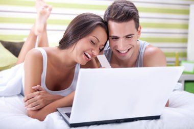 Couple in bed buying on-line with credit card clipart