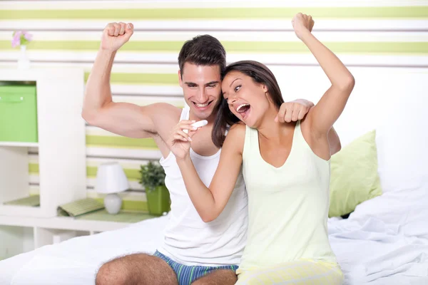 Happiness couple looking in pregnancy test sitting on bed — Stock Photo, Image