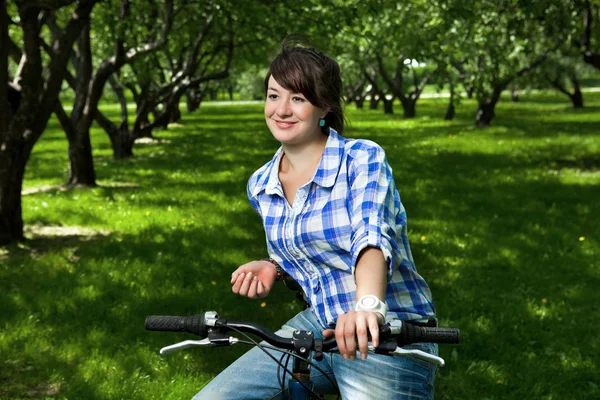 Молодая девушка на велосипеде в саду — стоковое фото