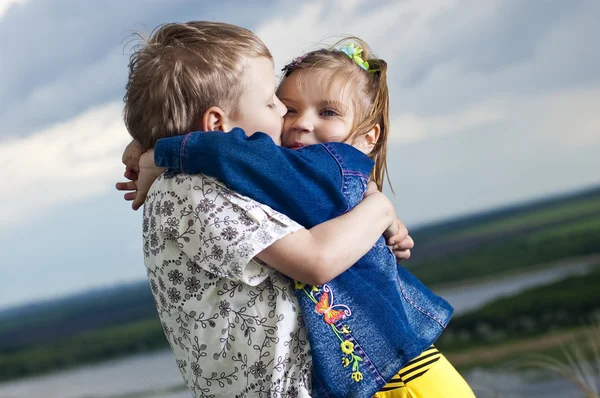 Pequeño niño y niña es besado en un fondo un paisaje — Foto de Stock