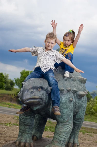 Lilla modiga barn på en dinosaurie i en park — Stockfoto