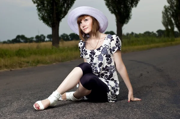 Mooi meisje zit in een hoed buitenshuis — Stockfoto