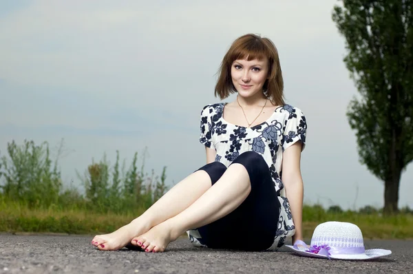 Vacker ung flicka sitter i en hatt utomhus — Stockfoto