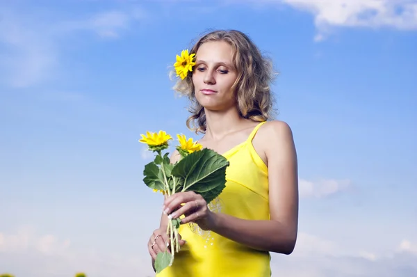 Beautiful young girl with sunflowers on a background clouds — Stock Photo, Image