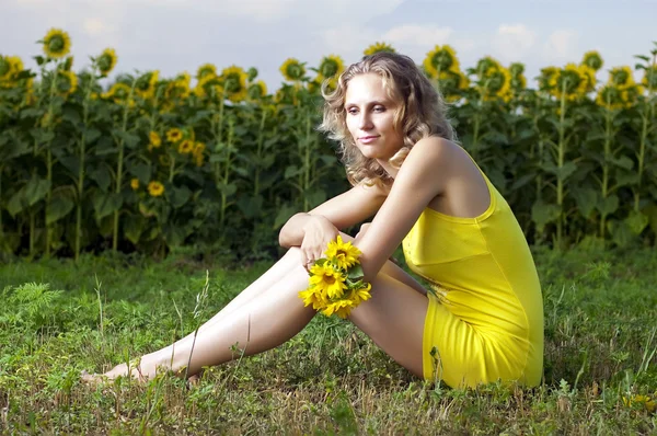 Sarı giysili güzel kızı alanında sunflowe ile oturuyor. — Stok fotoğraf