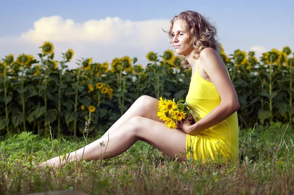 Menina bonita em roupas amarelas senta-se no campo com sunflowe — Fotografia de Stock
