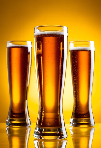Три стакана пива на желтом фоне — стоковое фото