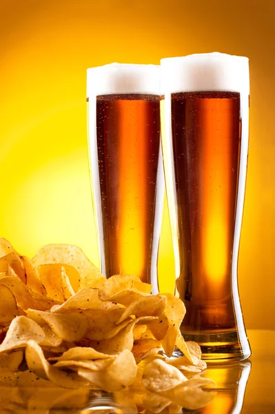Zwei Glas Bier und Kartoffelchips auf gelbem Hintergrund — Stockfoto