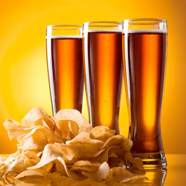 Три стакана пива и картофельные чипсы на желтом фоне — стоковое фото