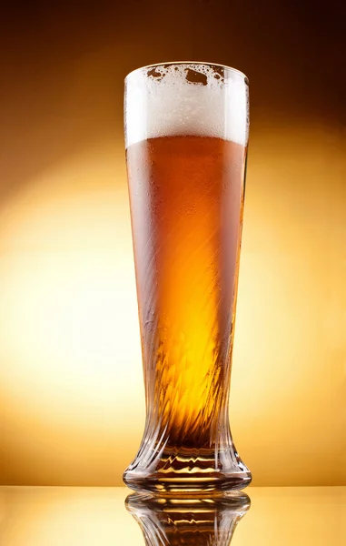 Frosty glass of light beer with froth over yellow background — Stock Photo, Image