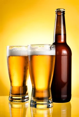 Two glasses and Bottle of fresh light beer on yellow background