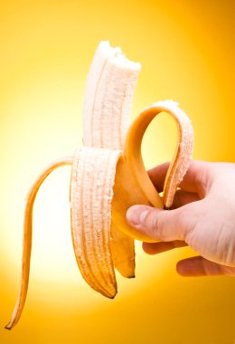 Hand holding peeled Bitten off banana over yellow background clipart