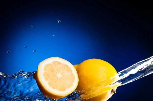 Fresh lemon and half of lemon in the splashes of water on a dark — Stock Photo, Image
