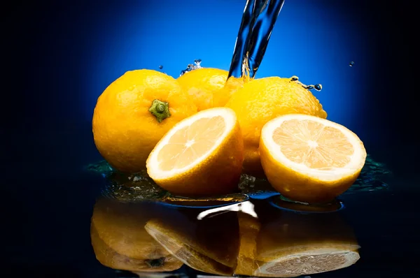 Fresh whole lemons and halves with a reflection in water on a na — Stock Photo, Image