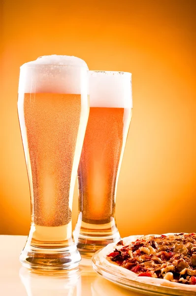 Dwa szklankę piwa i pizzy na żółtym tle — Zdjęcie stockowe