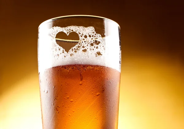 Glass of beer with the heart represented with froth close up ove — Stock Photo, Image