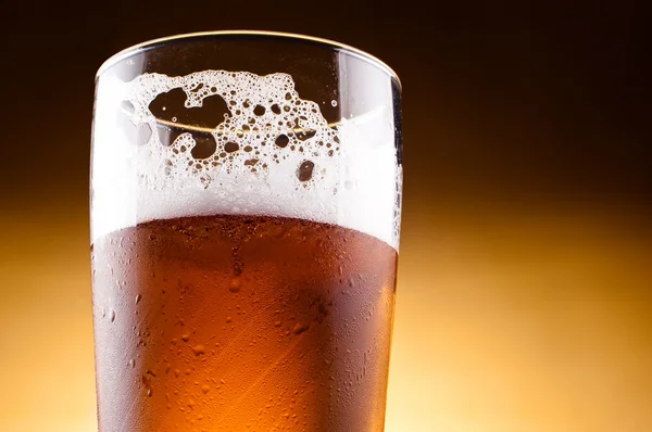 Glass of beer with froth close up on a yellow background — Stock Photo, Image