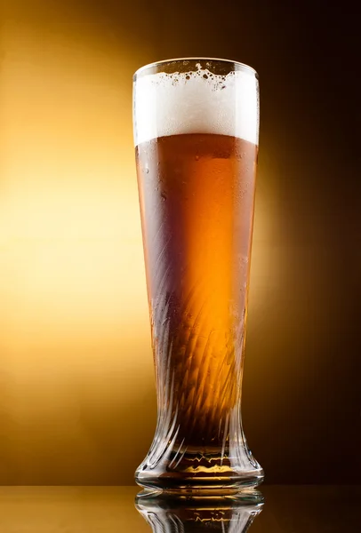Frostiges Glas helles Bier mit Schaum über gelbem Hintergrund — Stockfoto