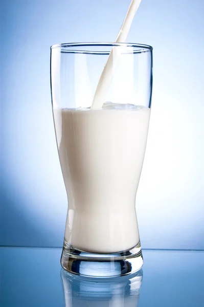 Ein frisches Glas Milch auf blauem Hintergrund gießen — Stockfoto